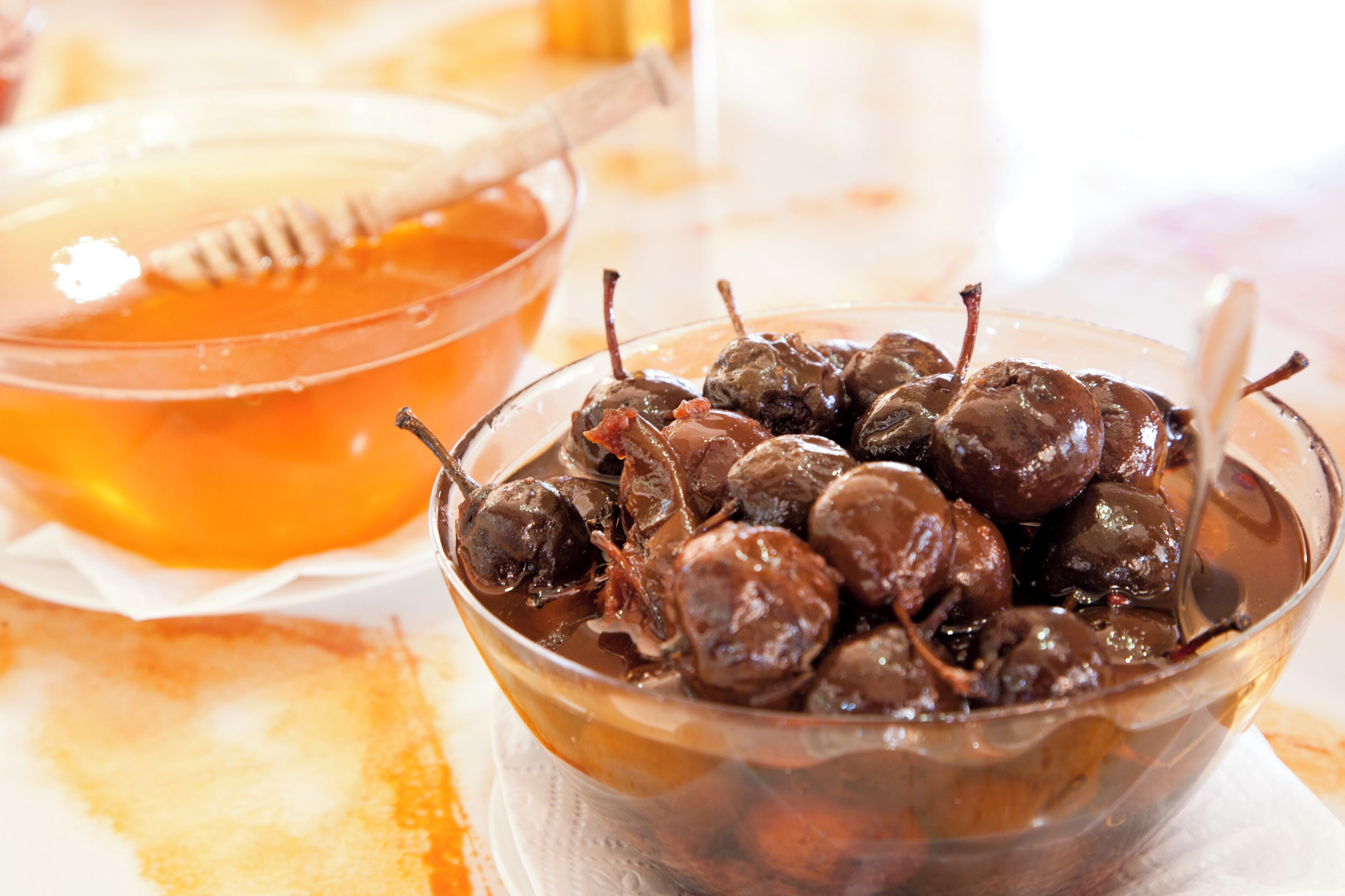 A bowl of chocolate-covered cherries with a honey dipper and a glass of honey.