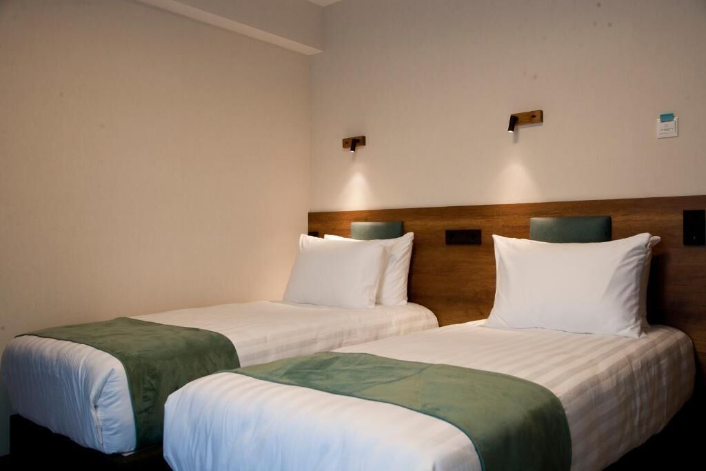 A hotel room with two single beds, a wooden headboard, and a small wall-mounted light fixture.