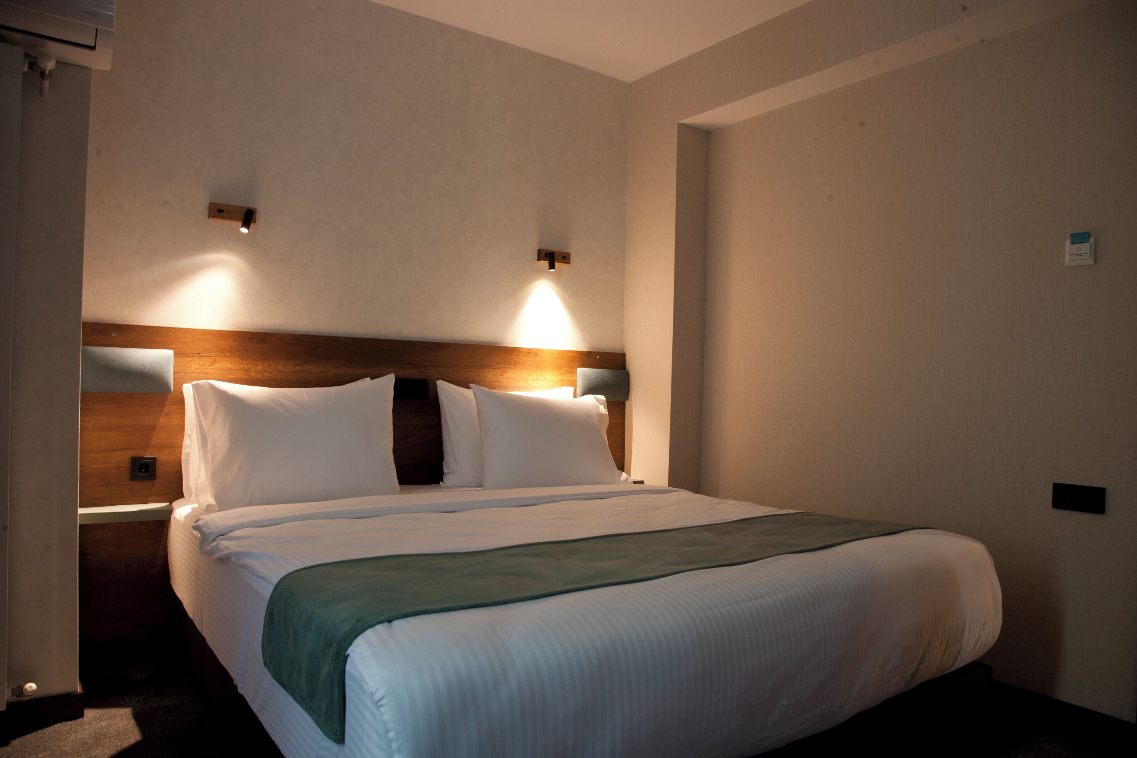 A hotel room with a bed, a nightstand, and a wall-mounted light fixture.