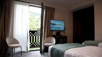 A hotel room with a bed, two chairs, a TV, and a view of greenery through a window.