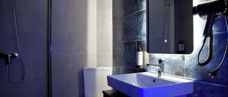 Un baño moderno con cabina de ducha de vidrio, inodoro blanco y un lavamanos grande con un espejo encima.