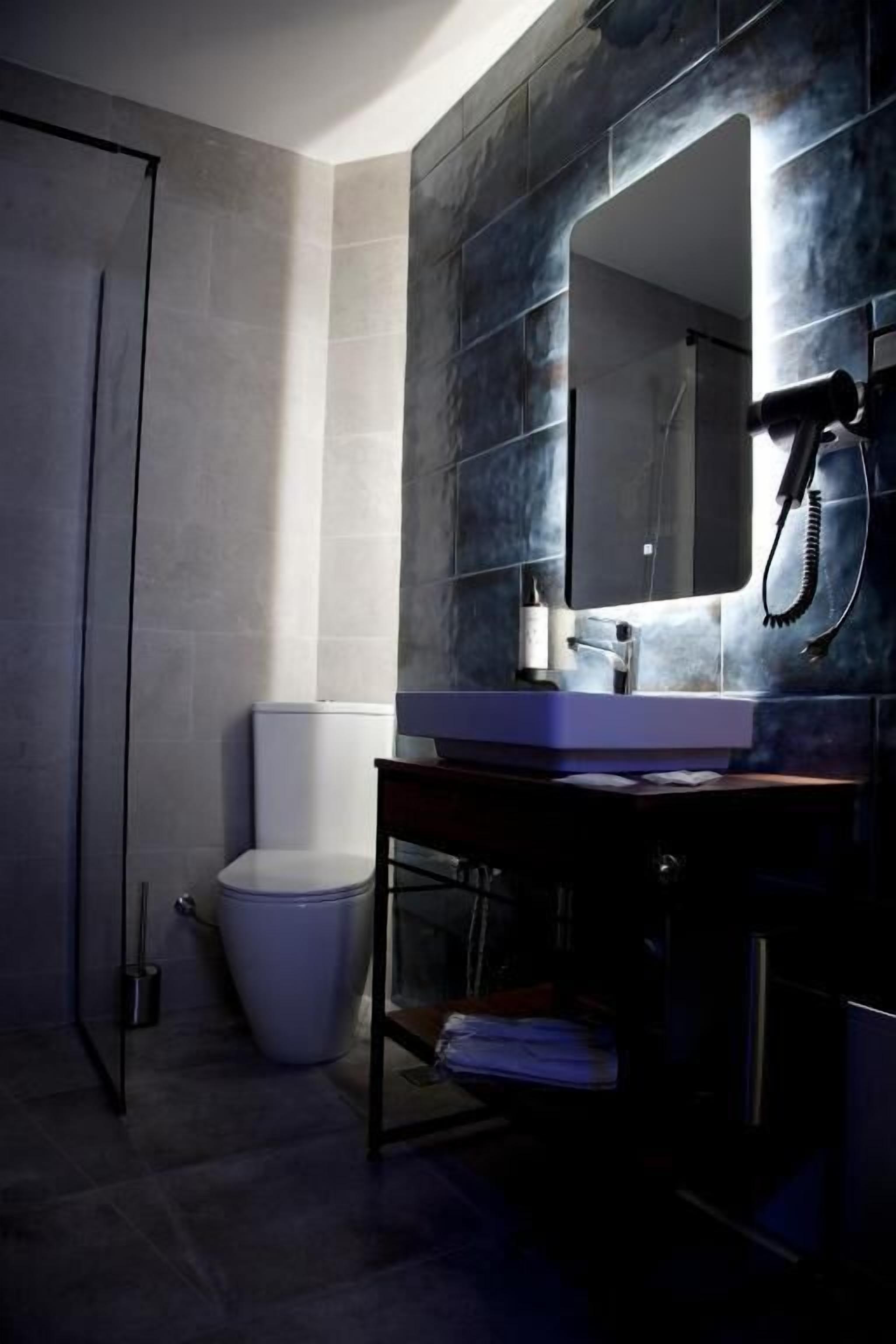 A bathroom with a white toilet, a sink with a mirror, and a hairdryer on a stand.