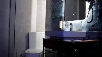 A bathroom with a white toilet, a sink with a mirror, and a hairdryer on a stand.