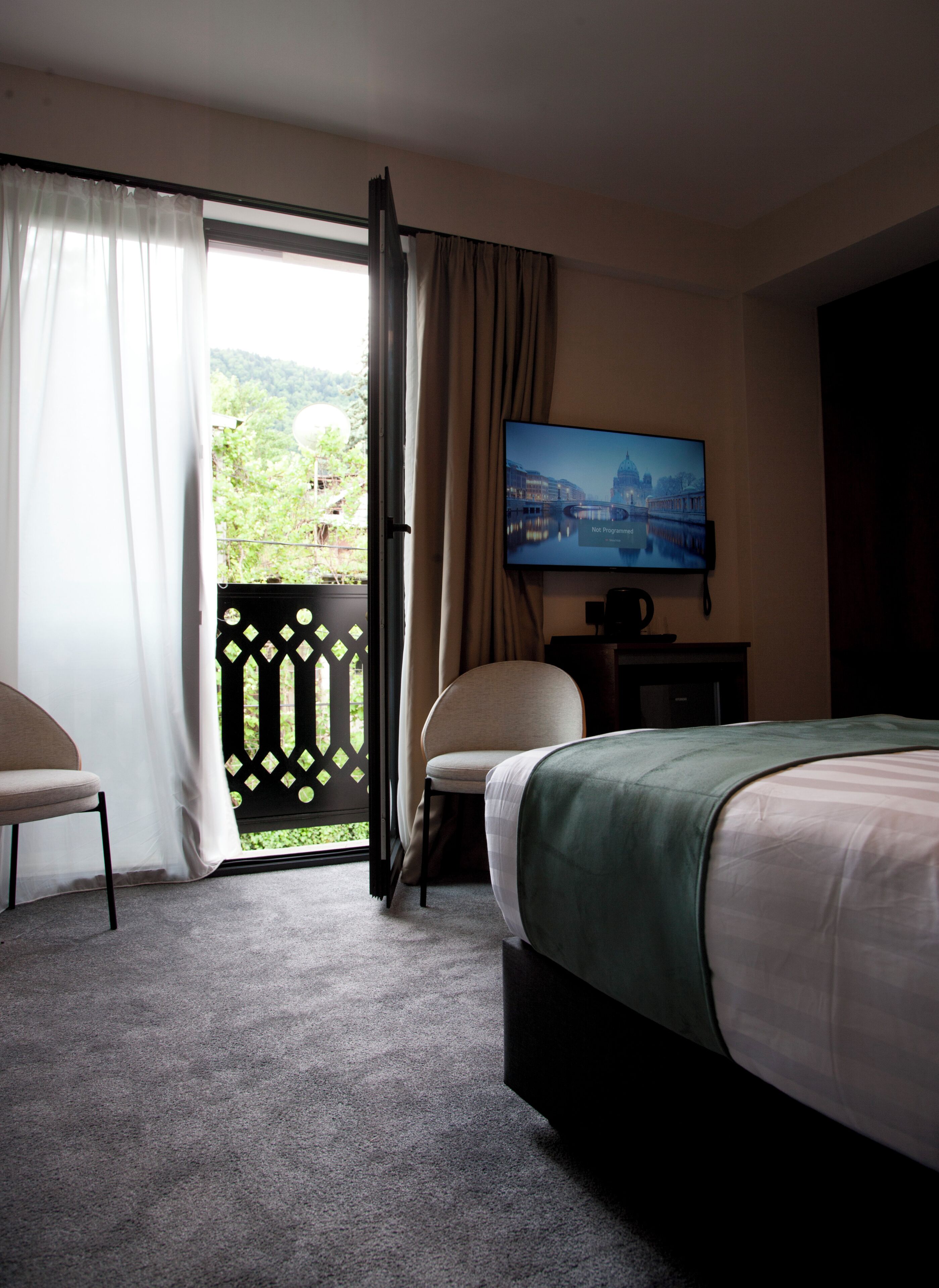 Habitación de hotel con una cama, una silla, un televisor montado en la pared y vistas a zonas verdes.