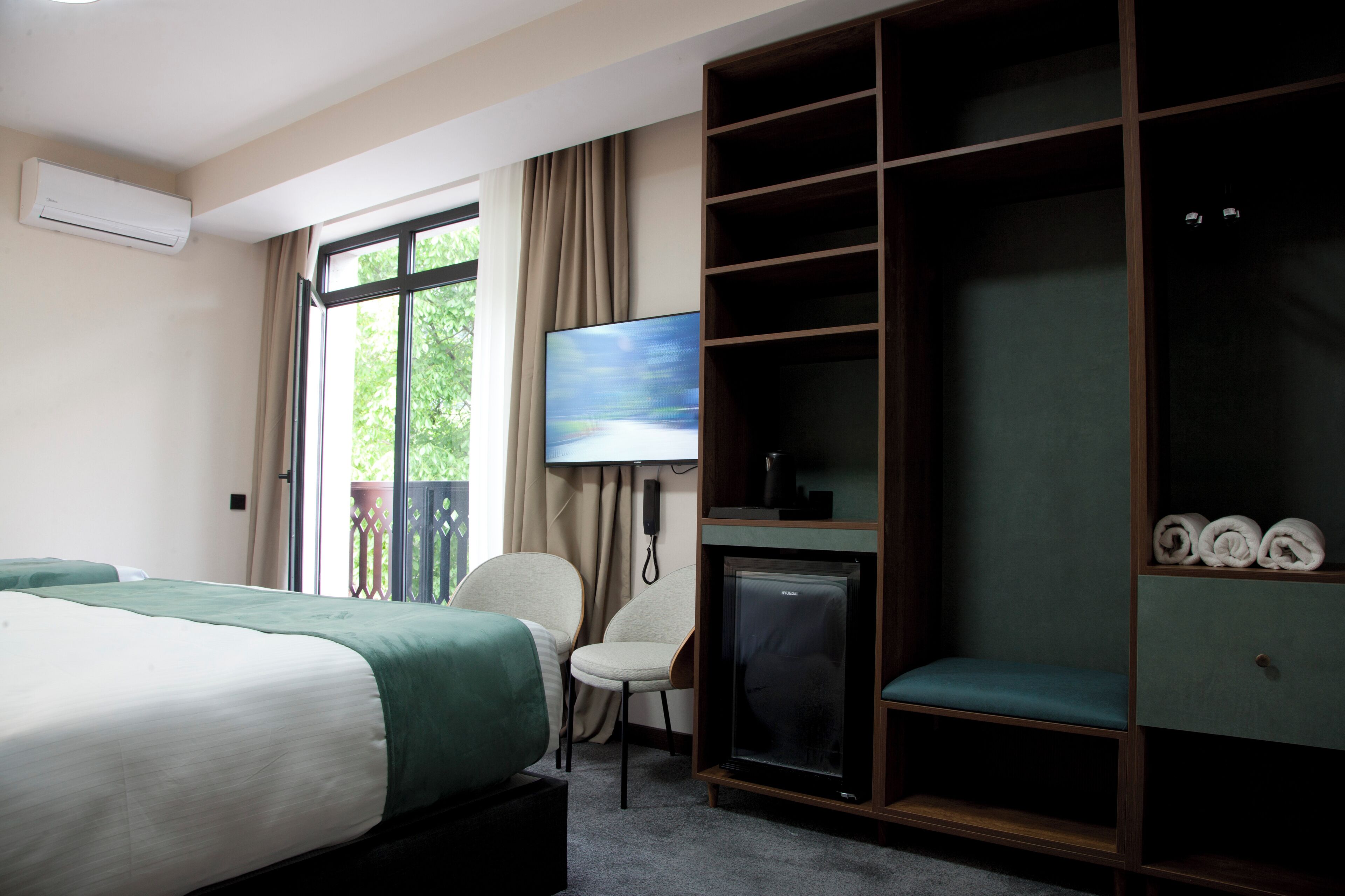 Ett hotellrum med en säng, en tv, ett skrivbord, en stol, en garderob och utsikt över grönområden utanför.