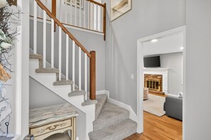 Eine Treppe mit weißen Geländern und Teppichstufen führt zu einem Wohnbereich mit Kamin.