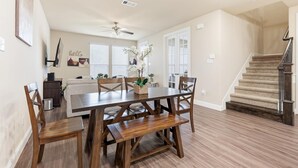 Un comedor con una mesa y sillas de madera, un ventilador de techo y una escalera.