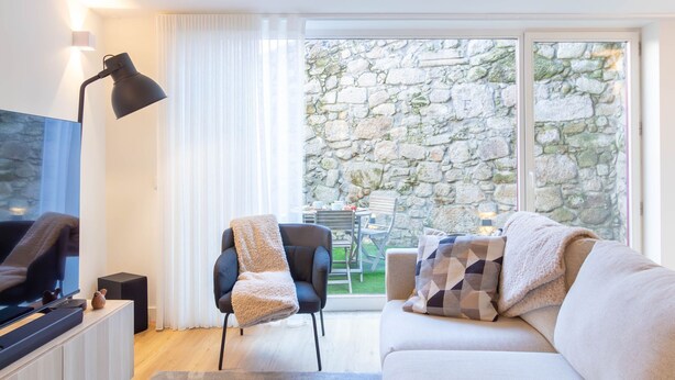 Een moderne woonkamer met een flatscreen televisie, een zwarte fauteuil, een witte bank en een stenen muur buiten.