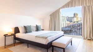 Een hotelkamer met een bed, nachtkastje, bankje en uitzicht op een historisch gebouw door een raam.