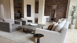 A modern living room with a grey sofa, a coffee table, and a small side table. There is a brick wall and a dining area in the background. - Spacious 4bedroom villa in tranquil La Quinta, private gated lake community (La Quinta)