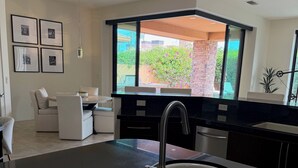 A modern kitchen with a black countertop, a wooden bowl of fruit, and a view of a brick wall and greenery outside. - Spacious 4bedroom villa in tranquil La Quinta, private gated lake community (La Quinta)