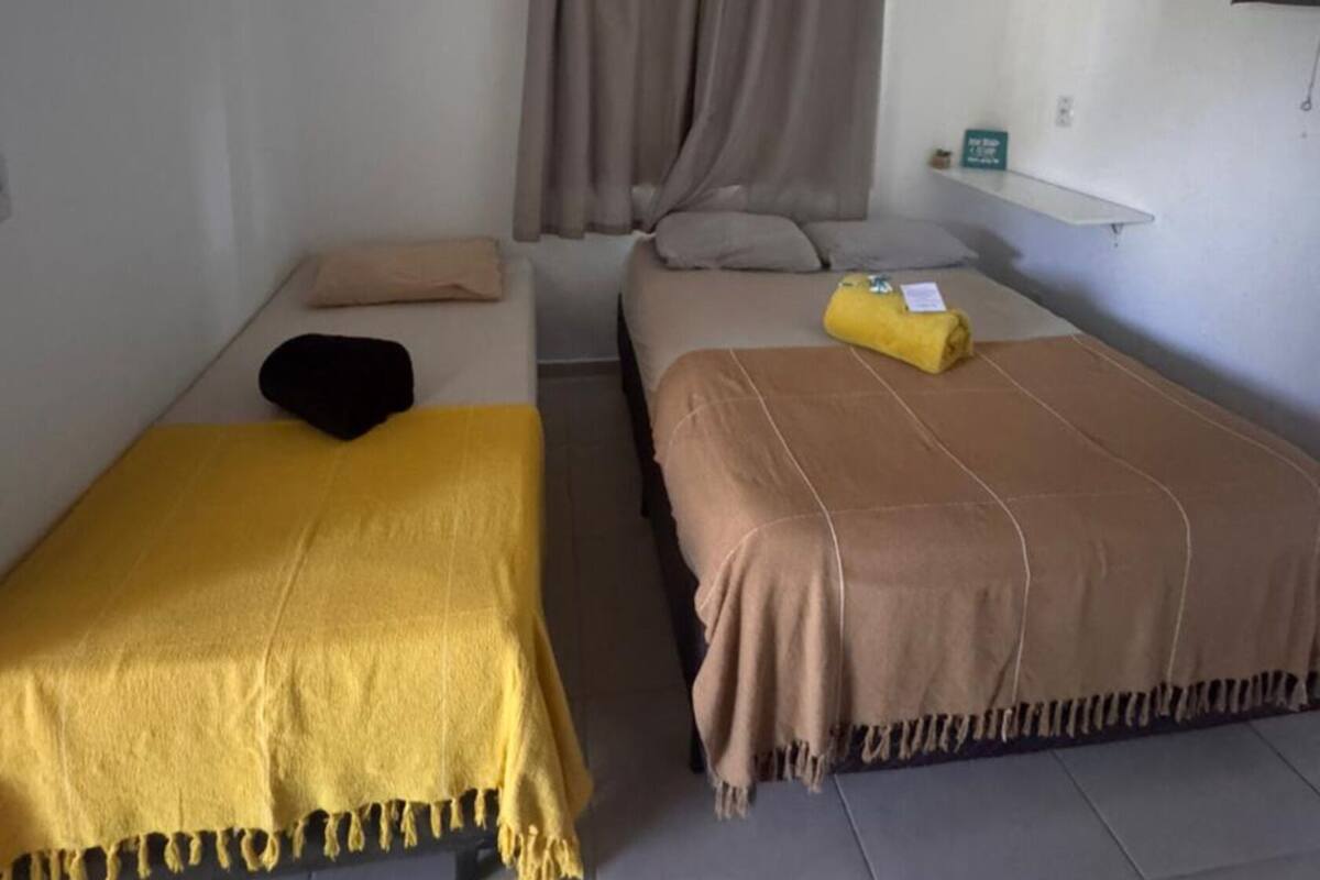 A room with two beds, a ceiling fan, an air conditioning unit, and a small shelf.