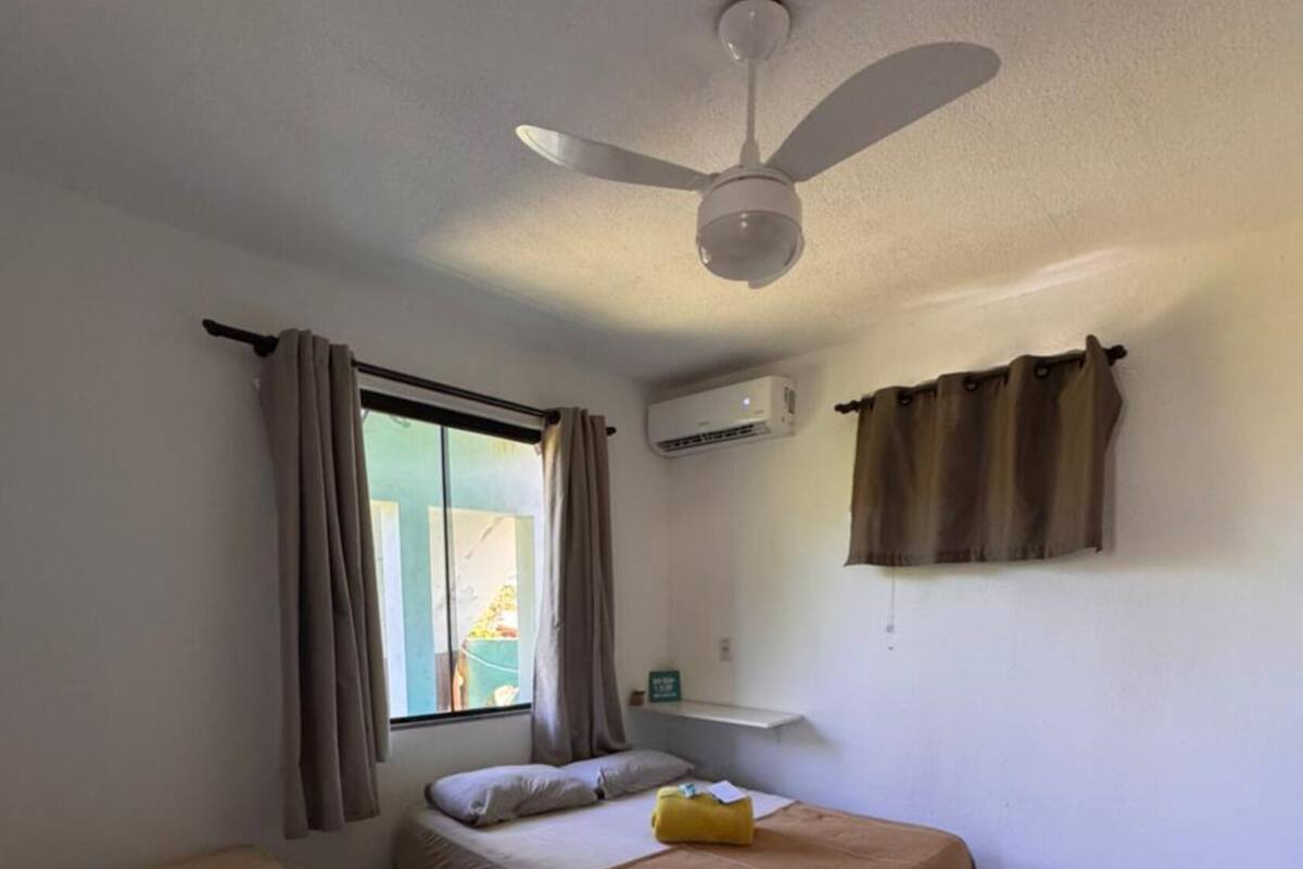 A room with two beds, a ceiling fan, an air conditioning unit, and a window with curtains.