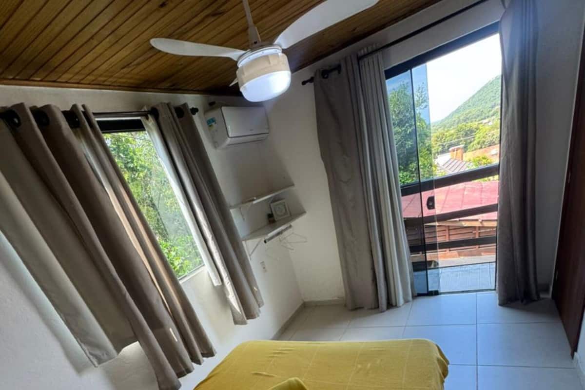 A bedroom with a bed, a ceiling fan, an air conditioning unit, and a view of the outdoors.