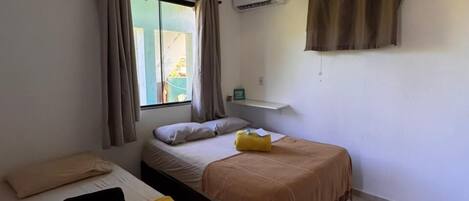 Quarto com duas camas, ventilador de teto, ar condicionado e janela com cortinas.
