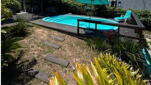 A backyard with a swimming pool, a covered patio area, and a small building. - Pousada Mahara (Imbituba)