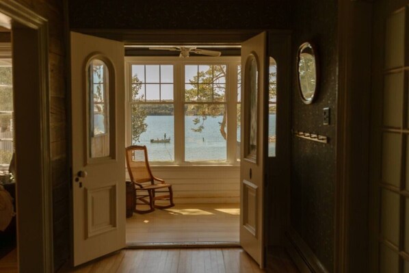 A room with a wooden floor, a chair, and a view of a lake through a window.