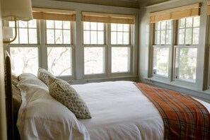 Un dormitorio con una cama grande, varias ventanas y vistas a árboles.