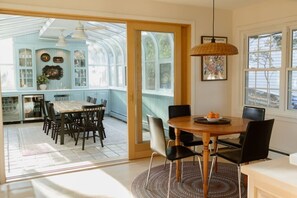 A room with a large window, a dining table, chairs, a ceiling fan, and a hanging light fixture.