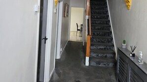 Un couloir avec un escalier, un lustre et une porte.