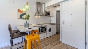Una cucina moderna con forno a microonde, forno e lavatrice, una zona pranzo con tavolo e sedie, e una porta bianca.
