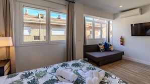 Una camera da letto con un letto, un divano, una televisione e una finestra che si affaccia su edifici.