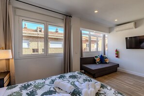 Une chambre avec un lit, un canapé, une télévision et une fenêtre donnant sur des immeubles.