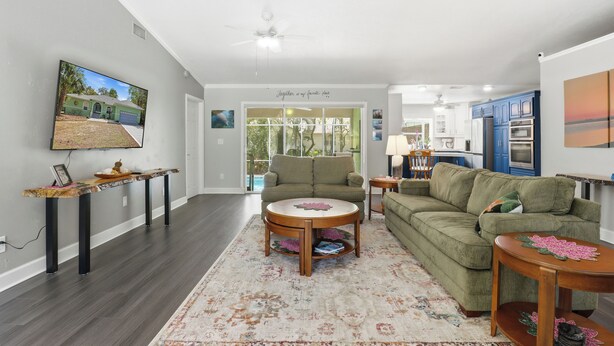 A living room with a sofa, coffee table, and TV mounted on the wall. - Hugh Bear Haven: Pool, Tiki Bar, Kayaks, Dog-Friendly (Crystal River)