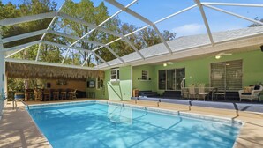 A swimming pool with a covered area, green walls, and outdoor furniture. - Hugh Bear Haven: Pool, Tiki Bar, Kayaks, Dog-Friendly (Crystal River)