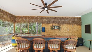 A bar area with a ceiling fan, wicker bar stools, and a view of the outdoors. - Hugh Bear Haven: Pool, Tiki Bar, Kayaks, Dog-Friendly (Crystal River)