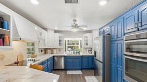 A modern kitchen with white and blue cabinets, stainless steel appliances, and a central island. - Hugh Bear Haven: Pool, Tiki Bar, Kayaks, Dog-Friendly (Crystal River)