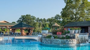 Ein Swimmingpool mit Liegestühlen, einer Laube und einem Wasserfall.