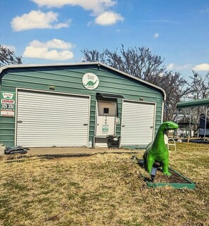 Un edificio verde con dos puertas de garaje cerradas, una pequeña entrada y una estatua de dinosaurio verde al frente.