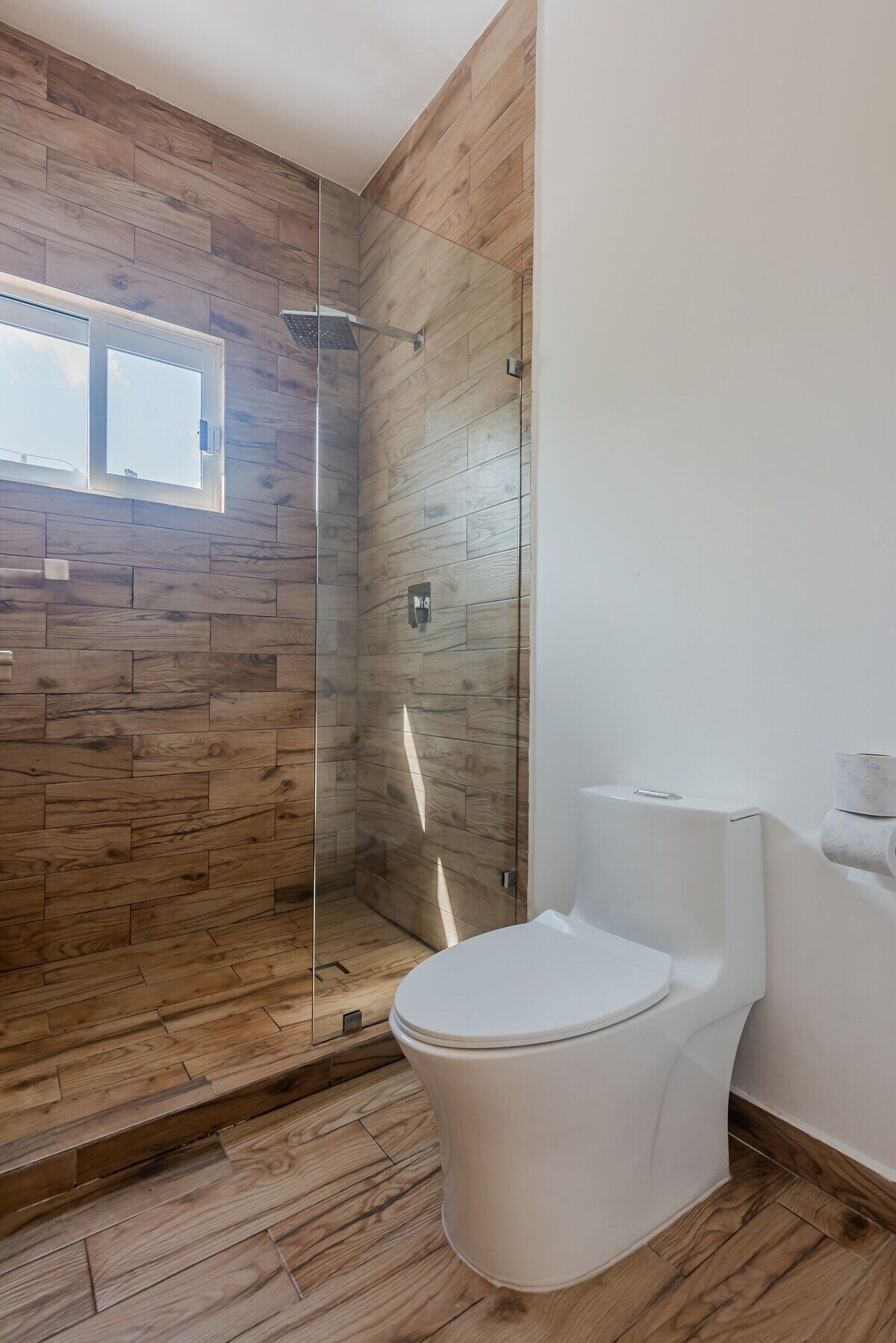 Un baño moderno con suelo de madera, cabina de ducha de vidrio y inodoro blanco.
