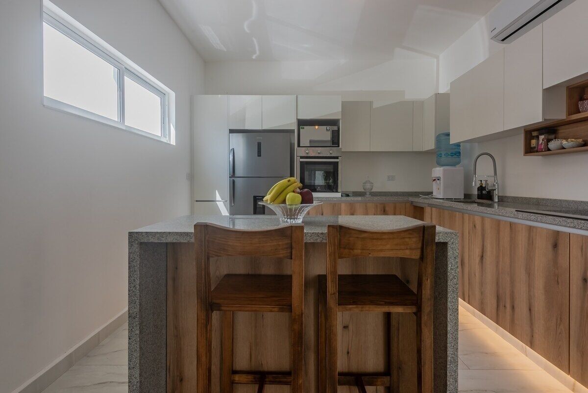 A modern kitchen with a central island, wooden bar stools, a refrigerator, oven, and a water dispenser.
