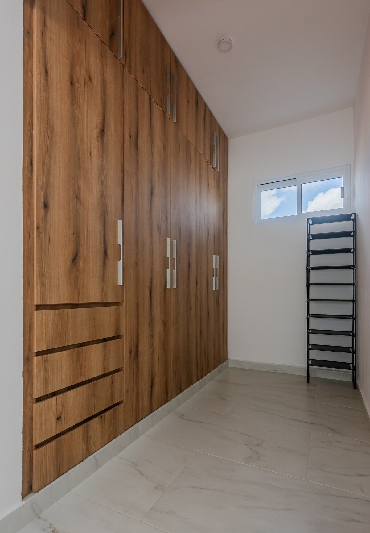 A room with a wooden wardrobe, a window, and a metal shelf unit.