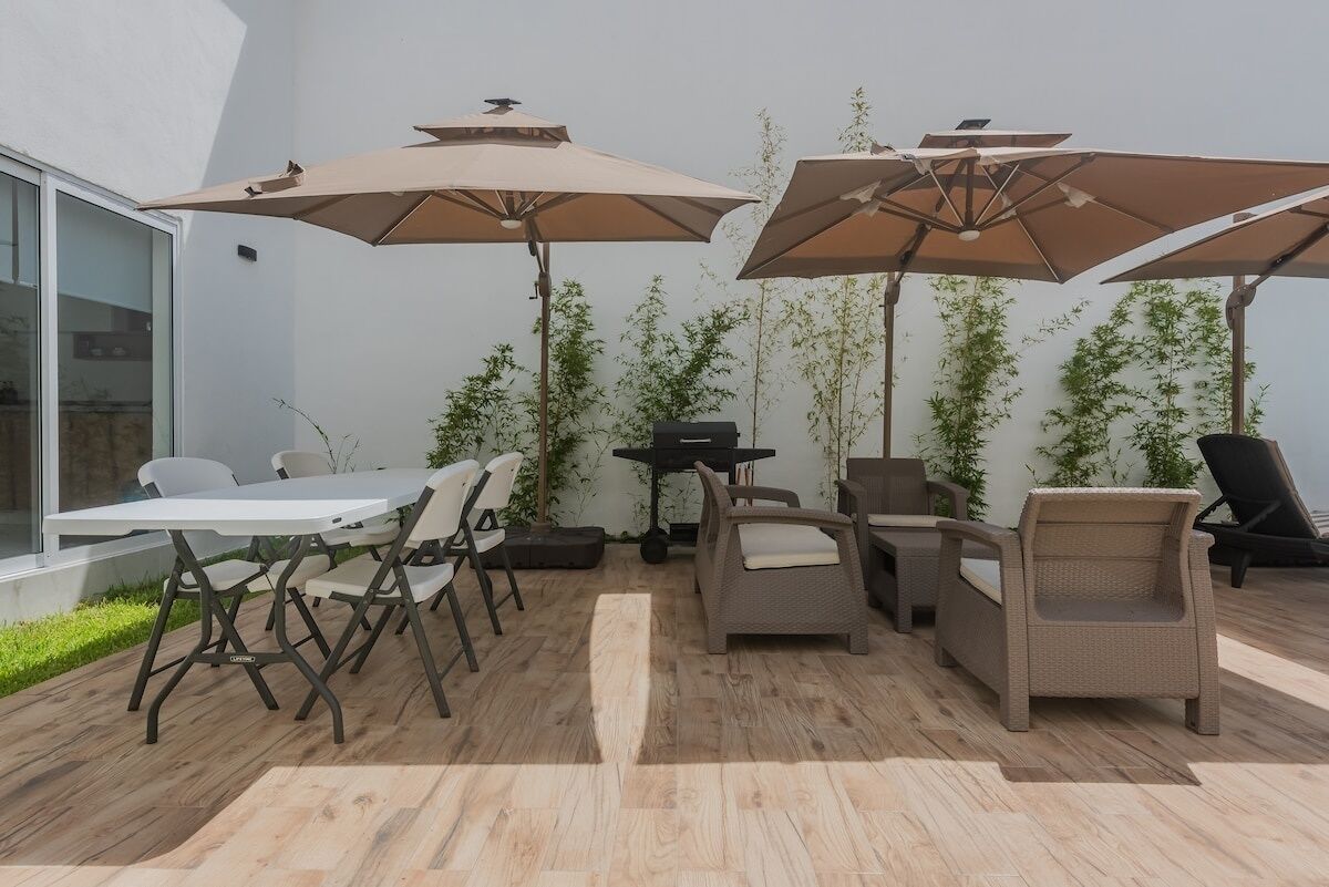 Une terrasse extérieure avec une table et des chaises, deux parasols et un barbecue.