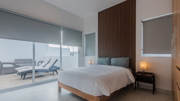 Ein Schlafzimmer mit Bett, Nachttisch und Blick auf einen Balkon mit Sitzgelegenheit.