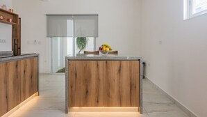 Eine moderne Küche mit Holzschränken und einer zentralen Kochinsel, einer Glastür, die auf einen Balkon führt, und Blick auf einen Baum.