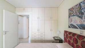 Quarto com cama, guarda-roupa, mesa de cabeceira, luminária e um quadro na parede.