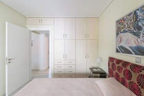 Ein Schlafzimmer mit einem Bett, einem Kleiderschrank, einem Nachttisch, einer Lampe und einem Bild an der Wand.