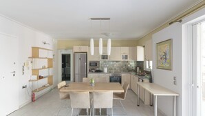Cozinha moderna com área de refeições, eletrodomésticos de aço inoxidável e piso ladrilhado em tons claros.
