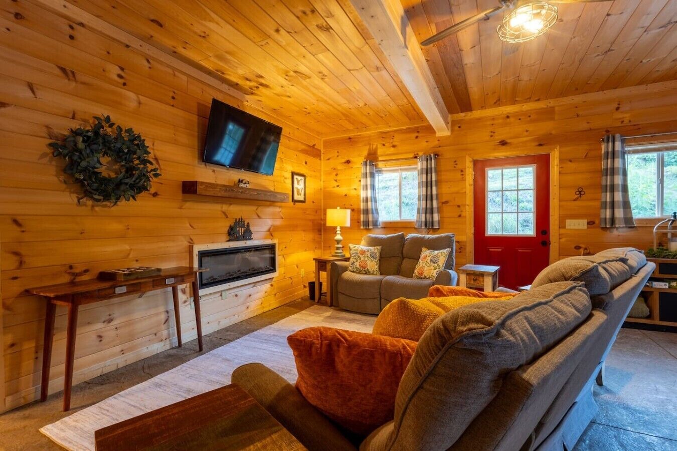 Interior acogedor de una cabaña con chimenea, televisor, sofá y una puerta roja.