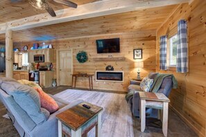Ein gemütliches Blockhaus-Interieur mit Kamin, Holzwänden, Fernseher und Essbereich.