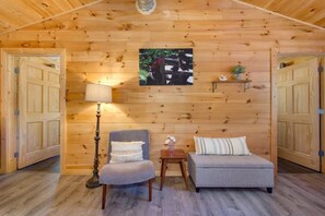 A cozy room with wooden walls, a single bed, a chair, a small table, and a lamp.