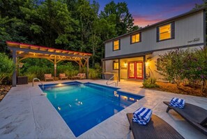 Una casa moderna con piscina, mobiliario exterior y porche cubierto.