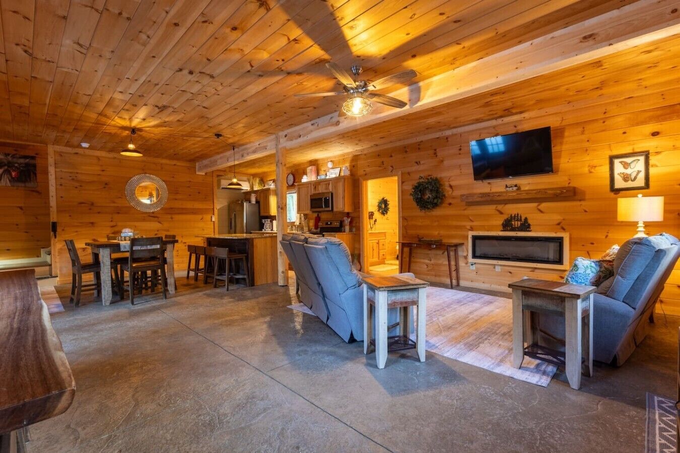 Interior de una cabaña de madera con comedor, sof á, televisor y ventilador de techo.