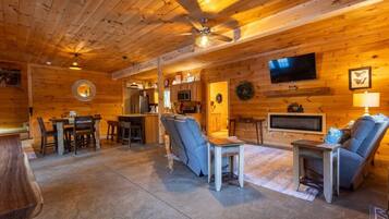 A log cabin interior with a dining area, a sofa, a TV, and a ceiling fan.
