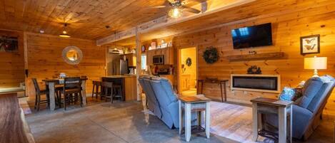 A log cabin interior with a dining area, a sofa, a TV, and a ceiling fan.