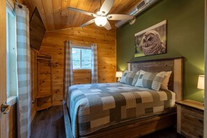 A bedroom with a wooden ceiling, a bed with a quilt, a ceiling fan, a window with curtains, and an owl painting on the wall. - 3BR Modern Farmhouse l Heated Pool, HotTub, Trails (Sevierville)